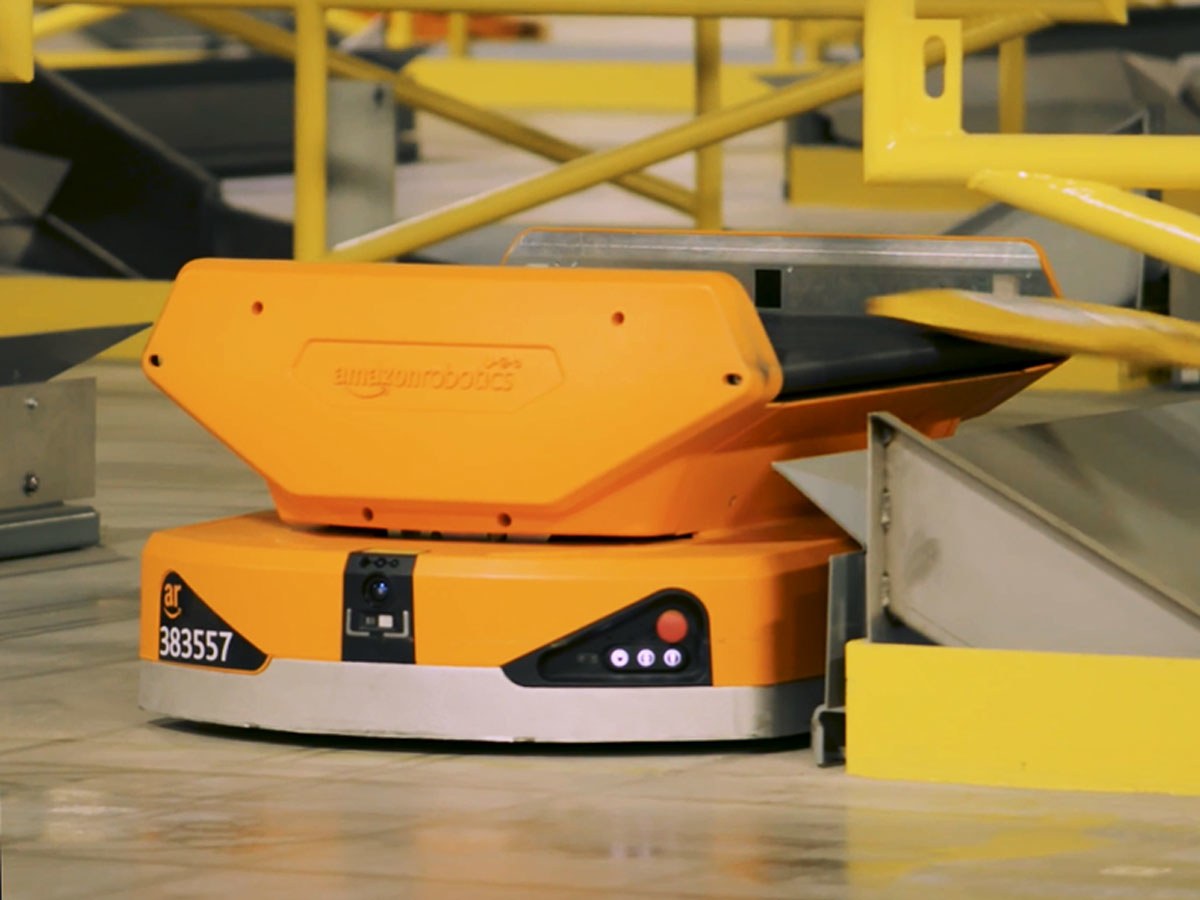 Robot arancione Pegasus di Amazon con nastro trasportatore che smista un pacco in magazzino
