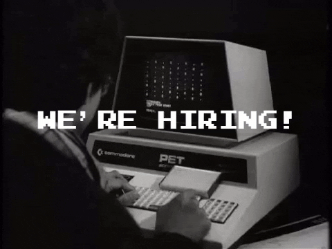 GIF animata retrò con la scritta “We're hiring!”, un uomo digita su un vecchio computer Commodore PET